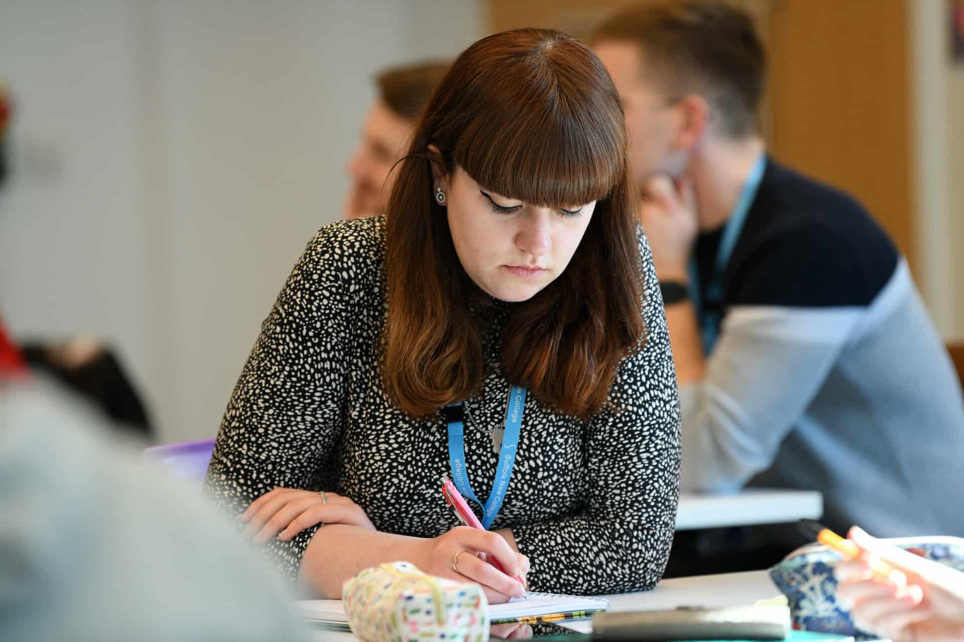 Female adult in a classroom setting making notes for their college course