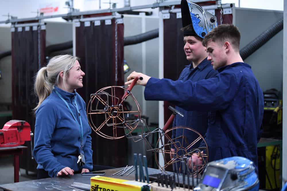 Two learners talking to a member of staff in the welding workshop.